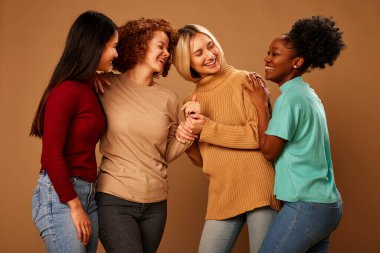 Multicultural girls with pure natural skin posing in studio and looking at the camera isolated on brown background.