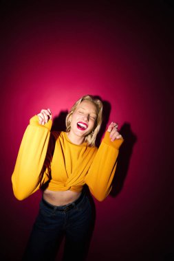 A joyful young blond woman is dancing isolated on magenta background. Viva magenta, color of the year.