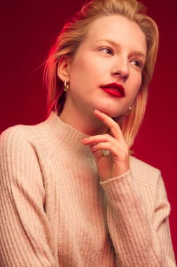 Studio shot of a serious blond woman posing on red background.