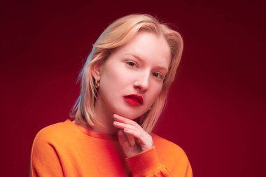 Studio shot of a serious blond woman posing on red background.