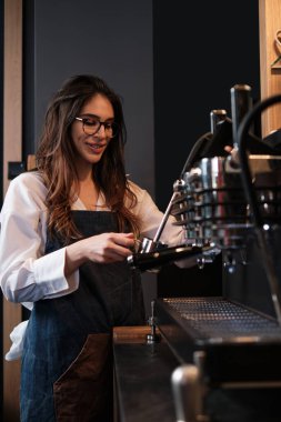 Barista kahve makinesinin yanında duruyor ve sütü ısıtıyor..