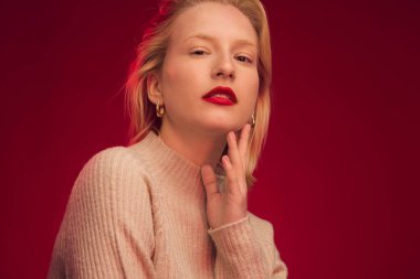 Studio shot of a serious blond woman posing on red background.