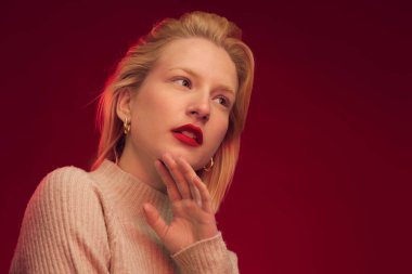 Studio shot of a serious blond woman posing on red background.