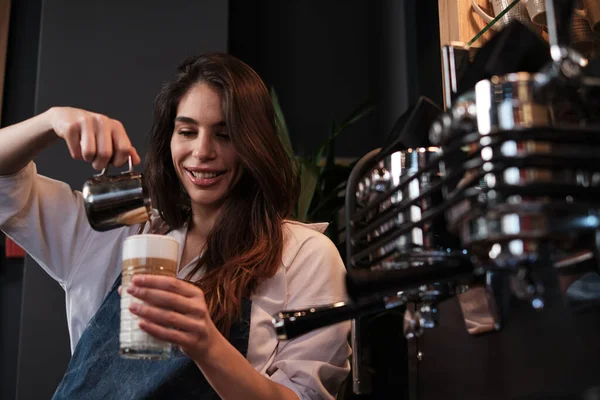 一位快乐的咖啡师一边站在咖啡店里一边用牛奶煮咖啡 一边举着杯子 — 图库照片