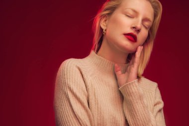 Studio shot of a serious blond woman posing on red background.