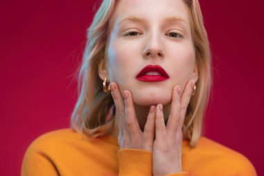 Güzel bir kadın, mor arka planda tek başına dikilirken yüzüne dokunuyor. Yaşasın mor, yılın rengi..