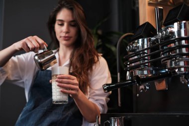 Kahve makinesinin yanında duran bardağa taze kahve hazırlayan ve süt ekleyen mutlu bir barista..