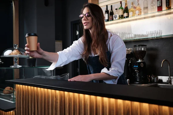 Barın arkasında durup müşteriye kahve veren dost canlısı bir barista..