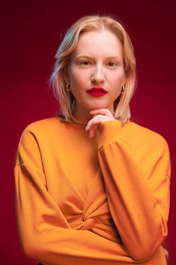 Studio shot of a serious blond woman posing on red background.