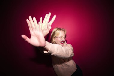 A cheerful young blond woman dancing in studio isolated on magenta background. Viva magenta, color of the year.