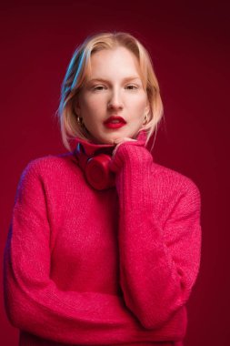 Sarışın, güzel bir kadın magenta arka planda, boynunda kulaklıklarla dikiliyor. Yaşasın mor, yılın rengi..