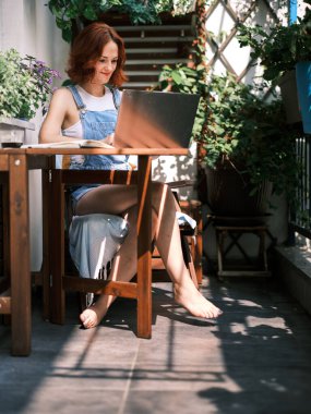 Bir kadın balkonda bitki yetiştiriyor, kentsel bir çevrede yeşil yaşamı besliyor.