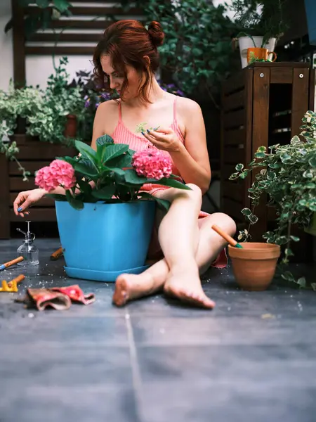 一个女人光着脚坐着 在一个蓝色的大水桶里种植着生机勃勃的粉红色花朵 周围是园艺工具 — 图库照片