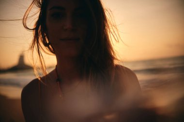 Gün batımında okyanusa bakan bir kadının arka plandaki görüntüsü gün batımının yansımasını ve ciddiyetini temsil eder.