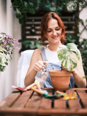 İçerik sahibi bir kadın, ahşap bir yüzey üzerinde aletlerle bahçe işleriyle uğraşırken gülümserken görülüyor.