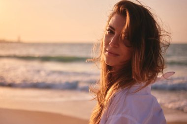 Gün batımında, yüzü okyanusa bakan bir kadının silüeti.