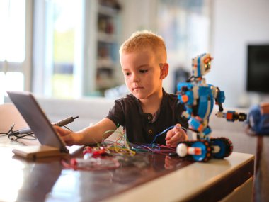Küçük bir çocuk, bir robot üzerinde çalışmak için çeşitli araç ve tellerle birlikte bir tablet kullanır, bu da kapalı alanda öğrenme ve yaratıcılığa pratik bir yaklaşım sergilemektedir..