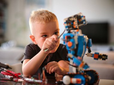Genç bir çocuk evdeki bir masada robotik projesini dikkatle gözlemliyor. Robot bilimine, teknolojiye ve pratik öğrenime büyük bir ilgi gösteriyor..