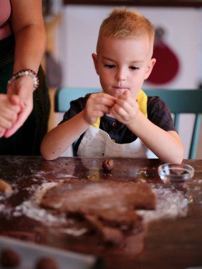 Önlüklü bir çocuk hamur şekline bürünür ve bir kadın gibi kurabiye pişirir, yaratıcılık, öğrenme ve aile bağlarını harmanlayan elle pişirme oturumunu yansıtır..