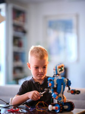 Genç çocukların yüzlerindeki ciddi bakış, mekanik mavi robotu dikkatlice tamir ederken yoğun odaklanma duygusunu ortaya koyuyor..