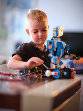 Düşünceli meşgul genç bir çocuk ince ayar yapıyor. Etrafa renkli kablolar saçan kurnaz mavi bir robot. Evde odaklanmış bir yaratıcılık ve yaratıcılık tablosu sunuyor..
