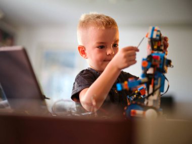 Renkli bir robotik cihaz yapmaya derinden odaklanmış küçük bir çocuk, bu güneşli günde sıcacık evde yaratıcı ve sabırlı bir atmosfer yaratıyor..