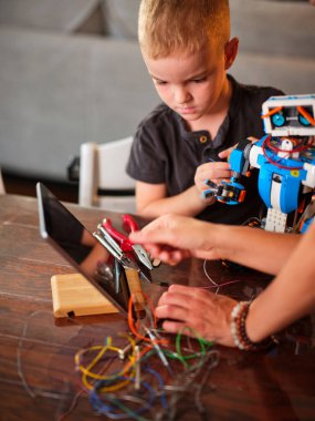 Resim, bir ebeveynin ve çocuğun bir robotu birleştirerek interaktif olarak öğrendiği, ortak eğitim deneyimleriyle oluşturulan bağı sembolize ettiği bir anı yakalıyor..