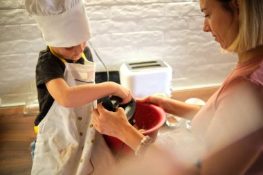 Beyaz önlük ve şapkayla süslenmiş genç ve hevesli bir aşçı, yanında bir yetişkinle harmanlanmış, sıcak, dağınık bir mutfak köşesinde asırlık bir bilginin geçişini simgeliyor..