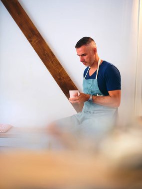 Mavi önlüklü rahat bir barista, elinde bir fincan kahve, kalabalık bir kahve dükkanının ortasındaki sakin ve huzurlu bir anı temsil ediyor..