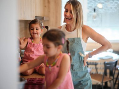 Küçük kız güneşli bir öğleden sonra sıcak bir mutfakta ailesiyle kek pişiriyor.