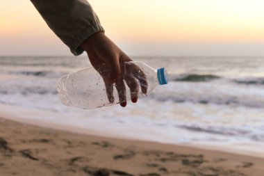 Plajda gün batımında gökyüzü olan plastik şişe atıkları taşıyan gönüllü bir el. Çevre bilimciler kirliliği azaltmak için çöpleri temizliyor, temizliyor ve deniz sahillerinde çöp topluyor.