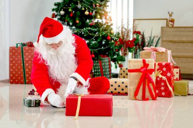 Mutlu Noel Baba, Noel hediyelerini paketliyor. Dekoratif Noel ağacının önünde, oturma odasında, Noel 'in mutlu kış tatilini kutluyor.