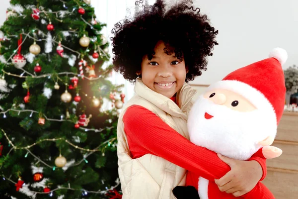 愛らしい笑顔の肖像黒カレーの髪を持つアフリカ系アメリカ人の女の子の子供装飾的なクリスマスツリーの下で巨大なクリスマス人形 子供は幸せなクリスマス冬の休日を祝う — ストック写真