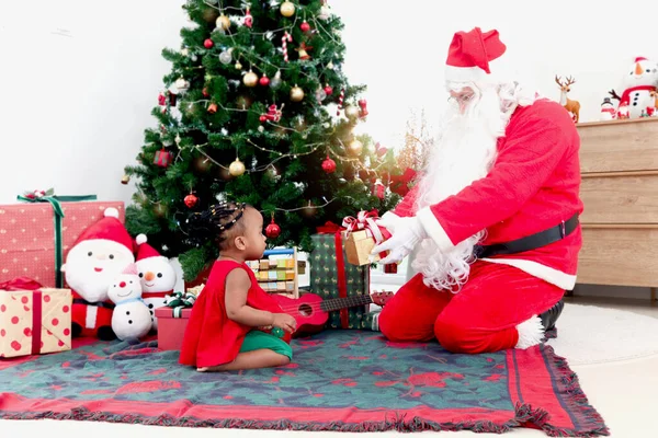 愛らしいアフリカ系アメリカ人の女の子の子供と装飾的なクリスマスツリーの下のサンタクロース サンタクロースはかわいい子供にプレゼントボックスを与え メリークリスマス冬の休日のお祝い — ストック写真