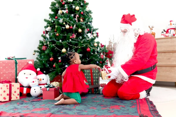 愛らしいアフリカ系アメリカ人の女の子の子供と装飾的なクリスマスツリーの下のサンタクロース サンタクロースはかわいい子供にプレゼントボックスを与え メリークリスマス冬の休日のお祝い — ストック写真