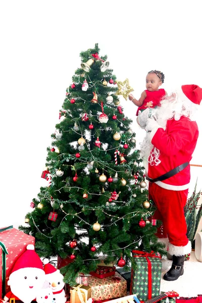 サンタクロースは愛らしいアフリカ系アメリカ人の女の子の子供を保持し 彼女が星でクリスマスツリーの上を飾るのを助ける メリークリスマス幸せな冬の休日のお祝い — ストック写真