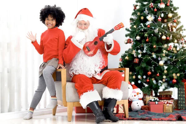 サンタクロースは幸せなアフリカ系アメリカ人のカレーヘアの女の子の子供がリビングルームで装飾的なクリスマスツリーの前でクリスマスの歌を歌い 幸せな冬の休日のお祝い — ストック写真