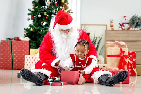 可爱的快乐微笑的非洲裔美国小女孩坐在圣诞树旁的圣诞老人身边 孩子打开圣诞礼物盒 感到惊讶和兴奋 — 图库照片