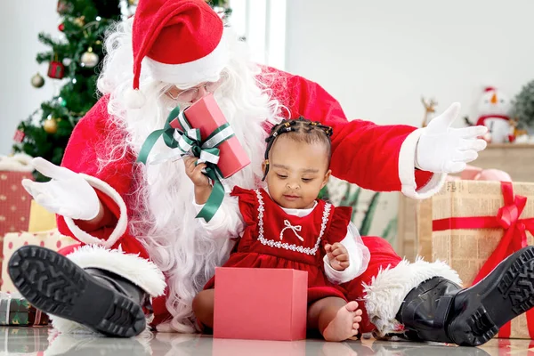 愛らしい笑顔アフリカ系アメリカ人の子供の女の子サンタクロースに座って装飾的なクリスマスツリーの周りにラップ 子供オープンクリスマスギフトボックスプレゼント 驚きと興奮を感じます — ストック写真