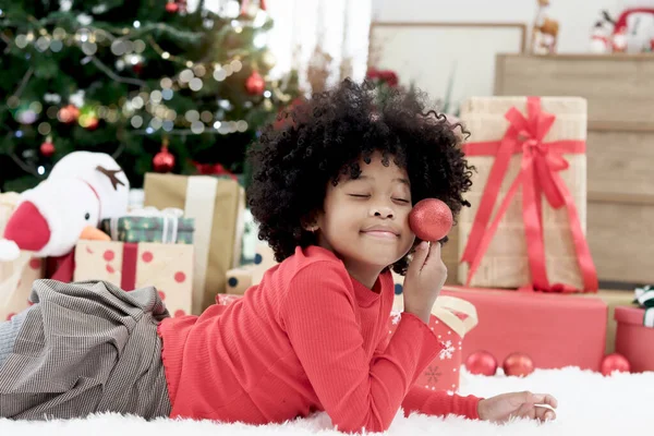 快適な幸せなアフリカ系アメリカ人の女の子黒いカレーの髪を持つ子供は リビングルームの床に白いカーペットの上に横になり クリスマスボールの装飾を保持し それに到達し クリスマス冬の休日 — ストック写真
