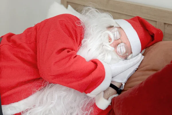Santa Claus sleeping comfortably, elderly senior old man with white long beard in Santa Claus costume taking a nap after working hard for a long time, happy Christmas winter holiday.