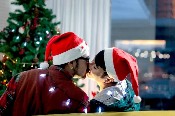 かわいい若いLgbtのカップルは キスの後ろからサンタの帽子を身に着けています クリスマス休暇に一緒に特別な瞬間を共有します ソファの上のゲイ男性恋人 クリスマス前の夜を祝います 冬のお祝い — ストック写真