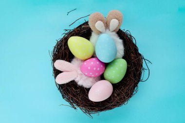 Top view of beautiful colorful Easter eggs wearing bunny rabbit ears headband in bird nest on blue background, decoration and celebration Easter and spring beginning.