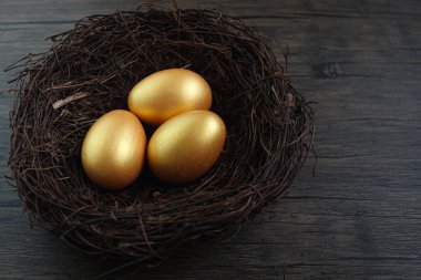 Top view of beautiful golden Easter eggs in bird nest on rustic brown wooden surface background, decoration and celebration Easter and spring beginning.
