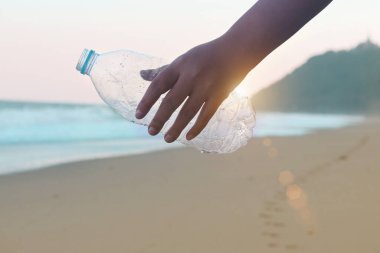 Plajda gün batımında gökyüzü olan plastik şişe atıkları taşıyan gönüllü bir el. Çevre bilimciler kirliliği azaltmak için çöpleri temizliyor, temizliyor ve deniz sahillerinde çöp topluyor.