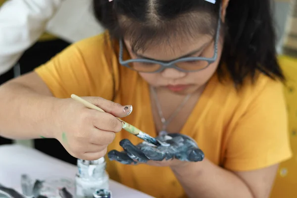 Happy children have fun with friends during study at school, girl with down syndrome concentrate painting on hand in art classroom, education of kids with physical disability and intellectual concept