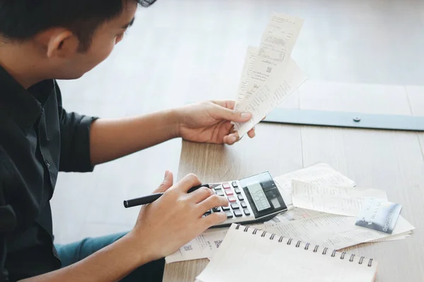 Young businessman in black shirt calculating his bill by using a calculator, thinking about his financial information and debt problems, want to reduce expenses and save money.