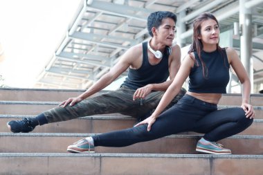 Genç koşucu erkek ve kadın aşık dışarıda birlikte egzersiz yapıyor, partner arkadaş koşucu dışarı çıkmadan önce merdivenlerde vücut esnetiyor, iki Asyalı koşucu sporcu antrenmanı yapıyor ve şehirde spor yapıyor.