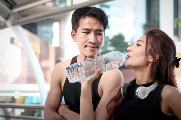 Happy smiling partner buddy runner man and woman lover resting after exercise run outdoor, sport girl runner jogger athlete holding drinking water bottle after training and doing workout in city.
