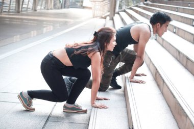 Genç koşucu erkek ve kadın aşık dışarıda birlikte egzersiz yapıyor, partner arkadaş koşucu dışarı çıkmadan önce merdivenlerde vücut esnetiyor, iki Asyalı koşucu sporcu antrenmanı yapıyor ve şehirde spor yapıyor.